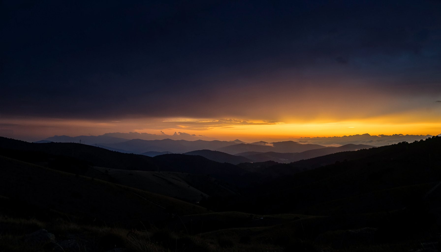 A dramatic dawn sky over rolling hills, deep navy fading into warm amber and gold at the horizon, conveying awakening and hope