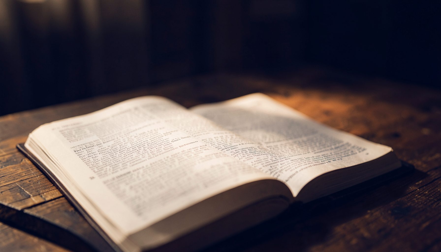 Open Bible on a wooden table in soft warm light, deep navy and amber tones, quiet contemplative atmosphere