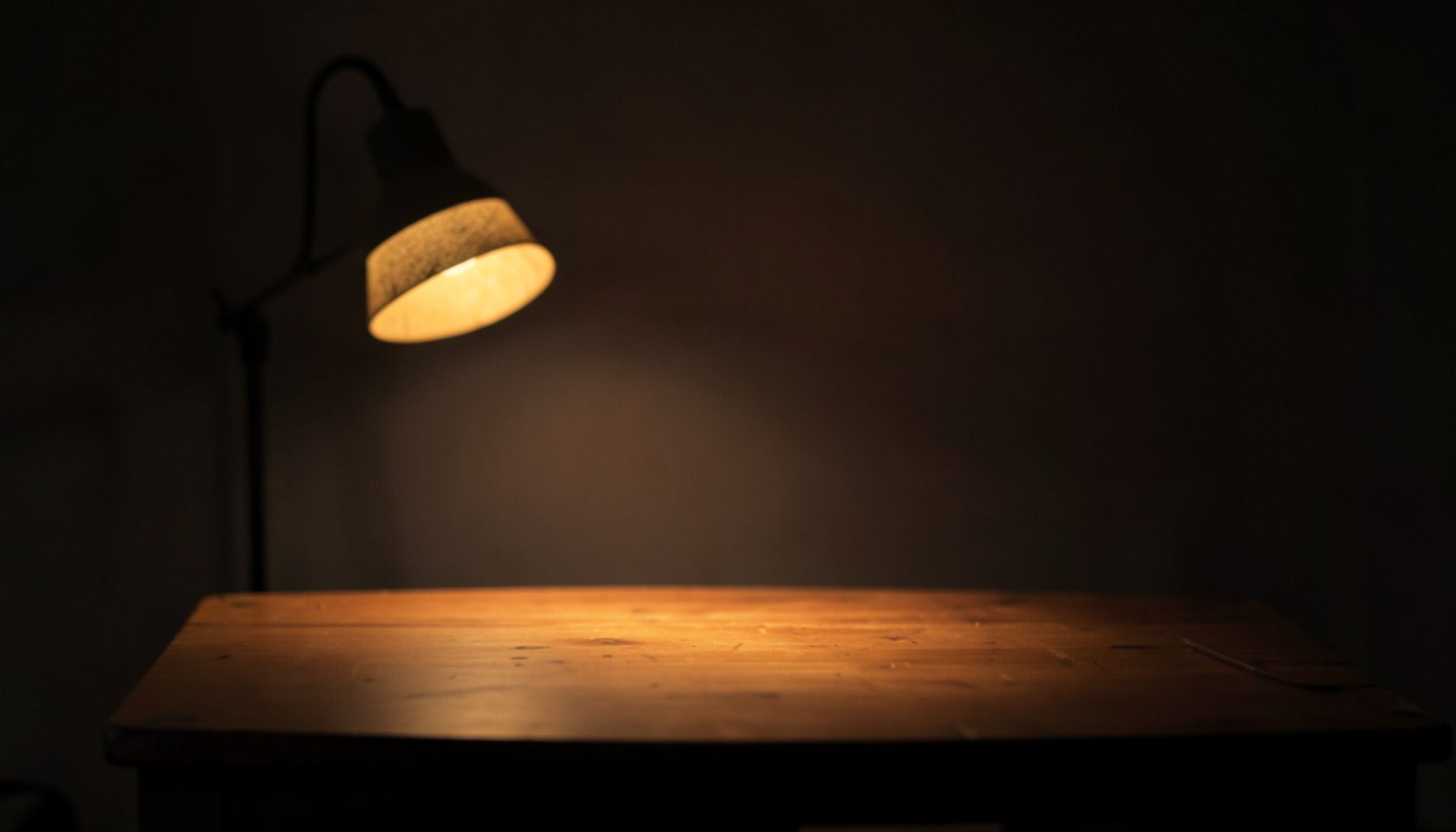 A dimly lit studio setting with a soft warm lamp glow and a simple wooden table, evoking a quiet, reflective atmosphere for video teaching